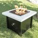A black and white square outdoor metal powdered coated fire pit table with flames set on an outdoor grassy lawn area