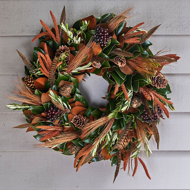 Decorative wreath with green leaves, brown feathers, and pinecones on a wooden background