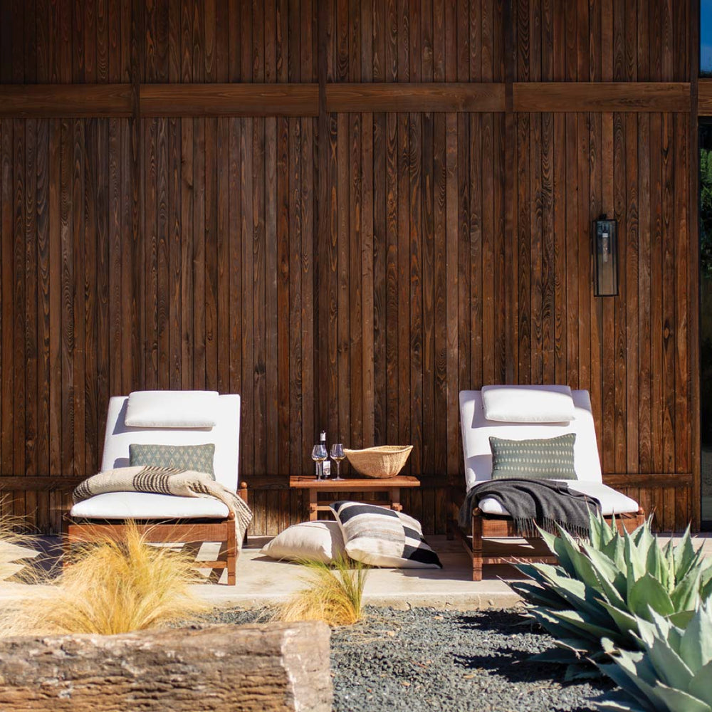 Pair of cushioned outdoor loungers with accent pillows and blankets, set against a wood backdrop in a modern desert garden.