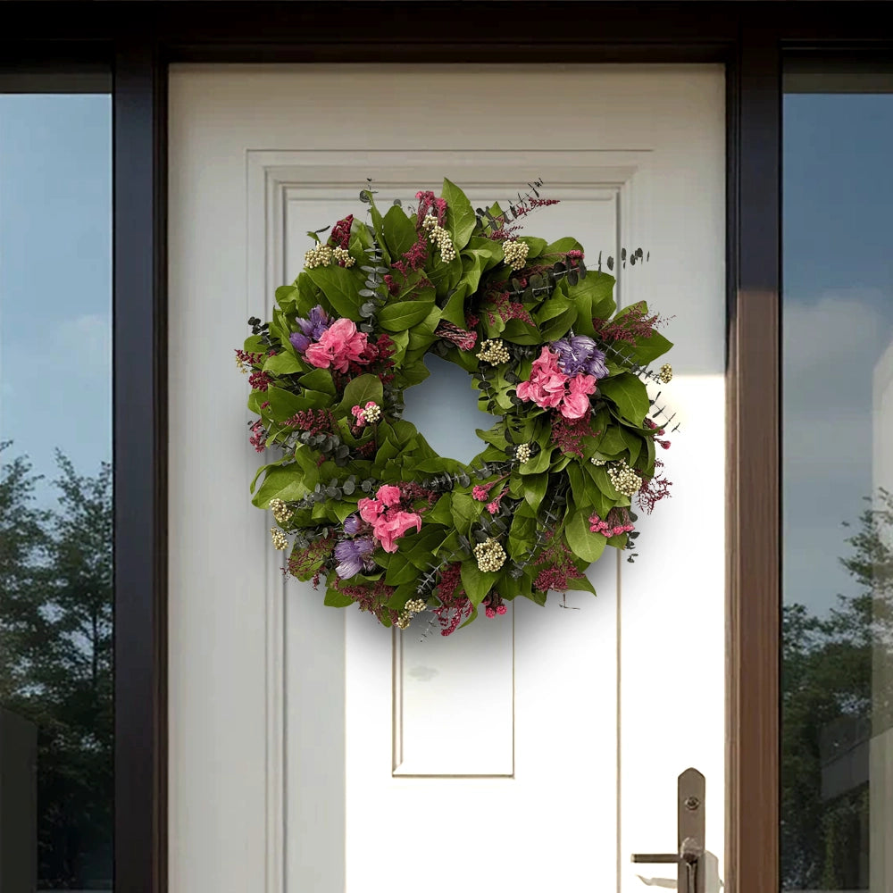 Green foliage wreath with pink, purple, and white flowers displayed on a white front door with side glass panels.
