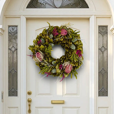 Festive spring wreath with dried flowers and colorful red-pink and green accents on a white door.