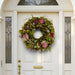 Festive spring wreath with dried flowers and colorful red-pink and green accents on a white door