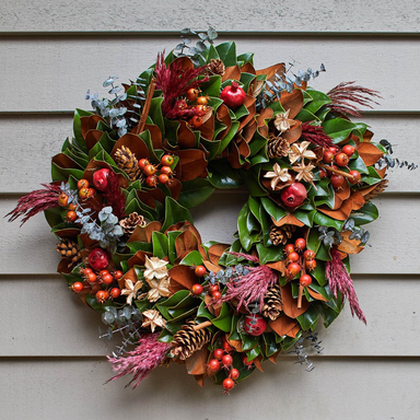 Decorative wreath with green leaves, red apples, and colorful berries on a wooden door.