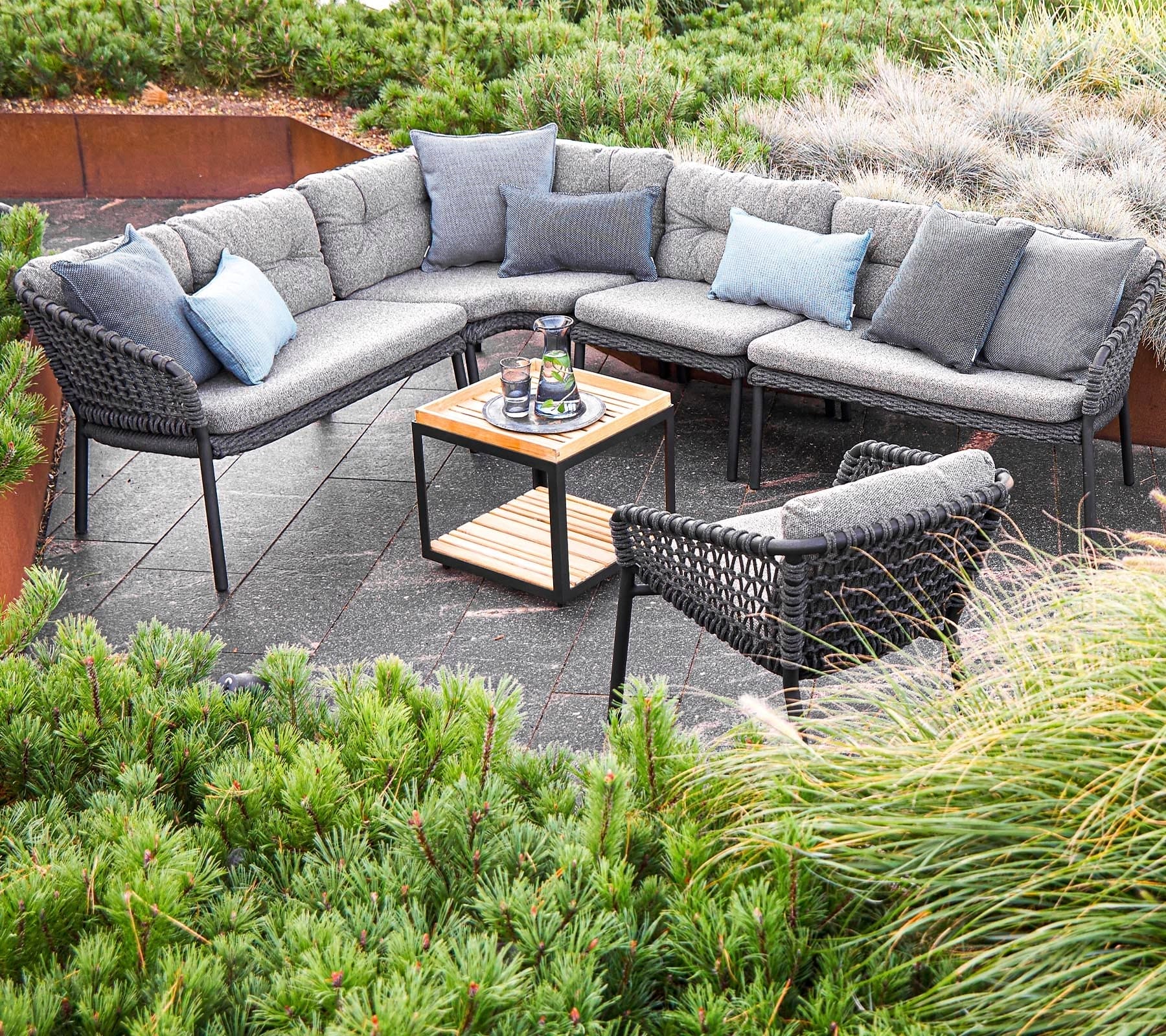 Boxhill's Ocean Outdoor Corner Sofa Module lifestyle image with other Ocean Module Sofa and Chair Collection, and Level Coffee Table with Teak top at patio