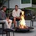 Boxhill's Cut High Outdoor Stool lifestyle image with 2 men sitting down and a fire pit in front