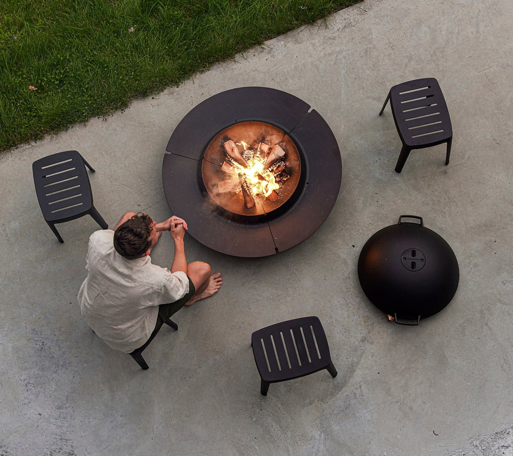 Boxhill's Cut High Outdoor Stool lifestyle image with a man sitting down and a fire pit in front, top view