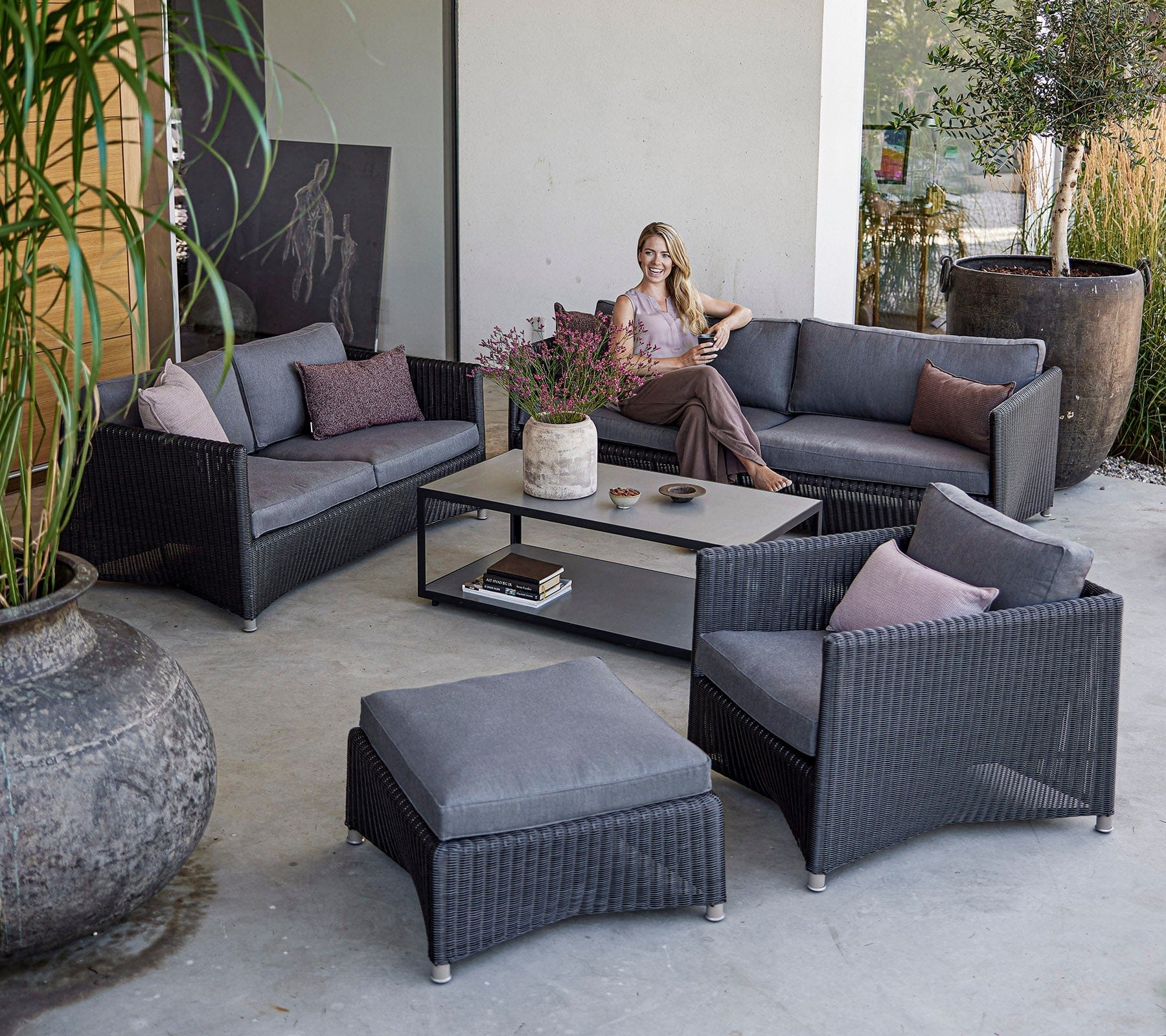 Boxhill's Diamond 2-Seater Weave Sofa lifestyle image with Diamond 3-Seater Weave Sofa, Diamond Weave Lounge Chair and Diamond Weave Footstool with a woman sitting down at patio