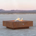 Corten steel square outdoor metal fire pits with lava rocks and flames placed on an outdoor area with a view of a distant mountain