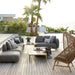 Boxhill's Capture Outdoor Corner Sofa w/ Table, Pouf, & Chaise lifestyle image on wooden platform beside the pool