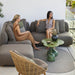 Boxhill's Glaze Outdoor Round Coffee Table lifestyle image on balcony with 2 women sitting down on a module sofa and Hive Outdoor Lounge Chair at the side