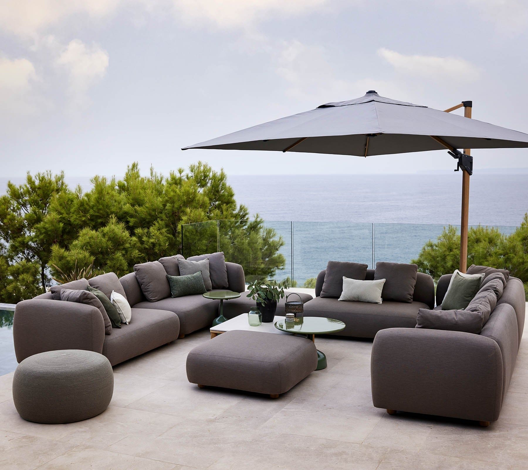 Boxhill's Capture Outdoor Pouf lifestyle image with Capture Module Sofa and Capture Coffee Table beside the pool with large umbrella shade