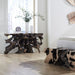 A modern room featuring a dark wood console table with a sculptural, branch-like base and a matching cowhide-textured bench in the foreground, set on light wood floors.