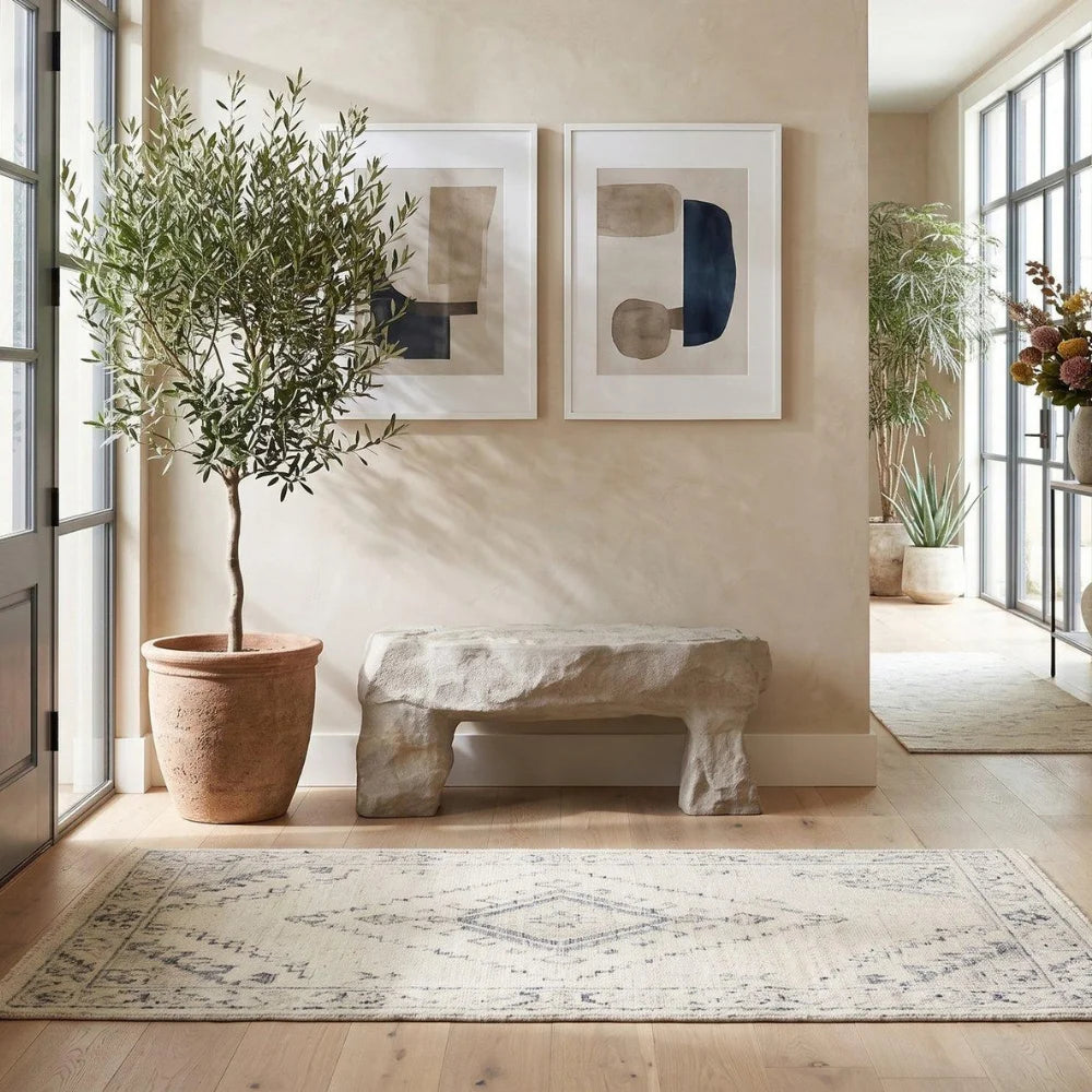 Cast Stone Outdoor Bench beneath abstract artwork beside a potted tree in a sunlit room.