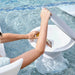 A person at a swimming pool uses a white side table with a gray with a small product package resting inside the open lid.