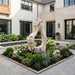Colossal Cast Stone Single-Hole Sculpture among flowers and greenery in a landscaped courtyard beside a pool.