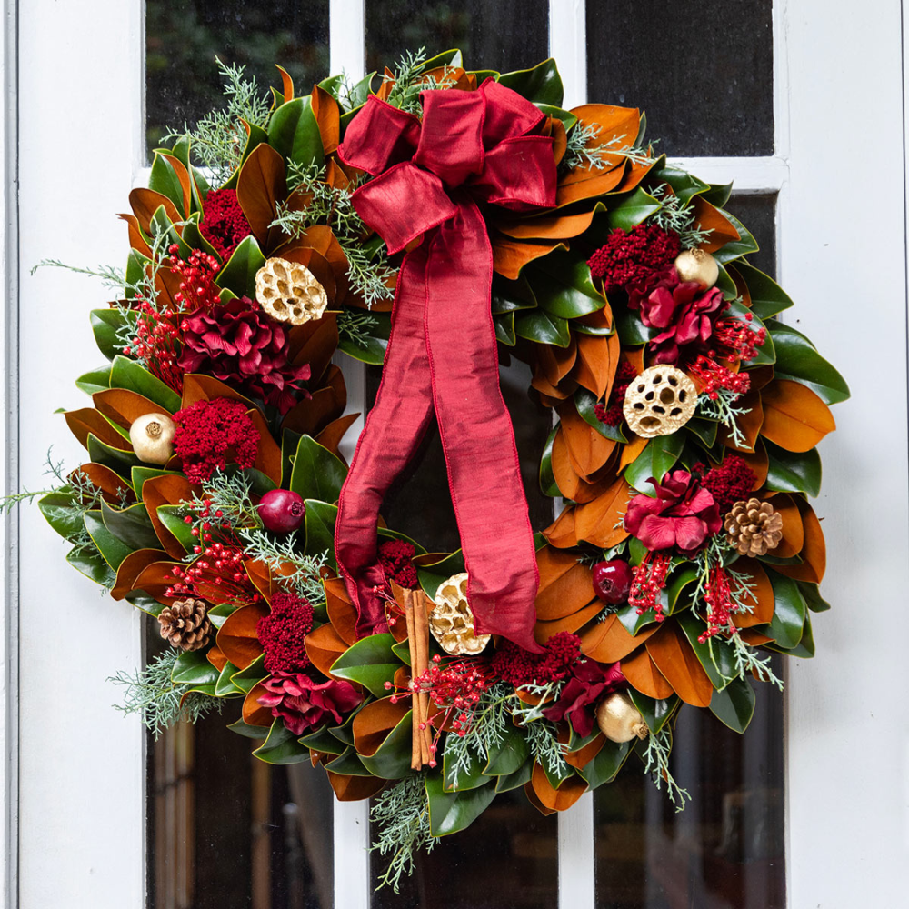 Decorative wreath with red bow and autumnal elements on a door.