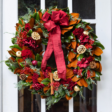 Decorative wreath with red bow and autumnal elements on a door.