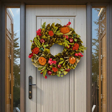 Festive wreath with orange, red, and green foliage and flowers hanging on a light gray wooden door with side glass panels.