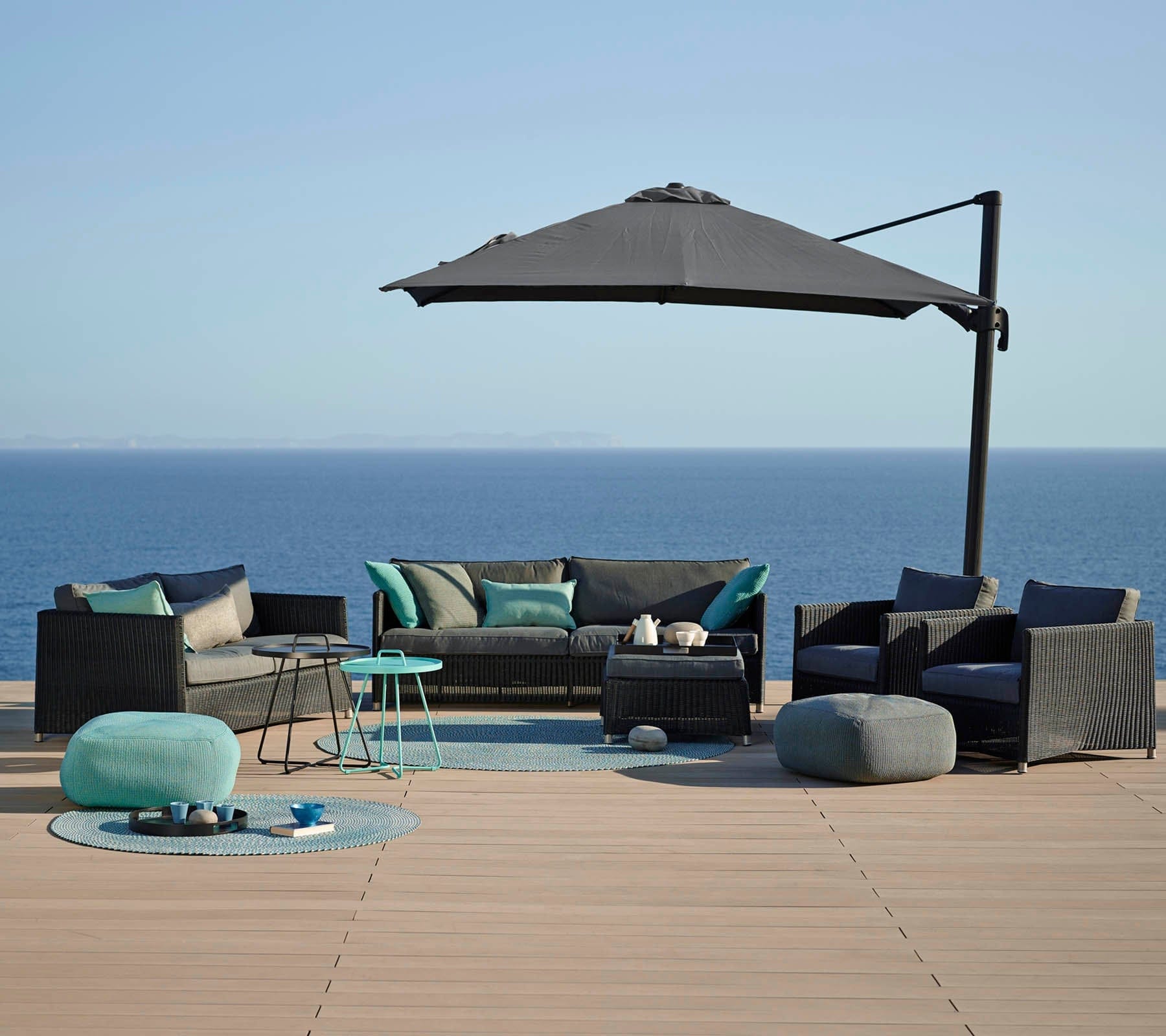 Boxhill's Diamond Weave Footstool with Cushion lifestyle image together with other Diamond Sofa collection and a parasol on wooden platform at seafront.