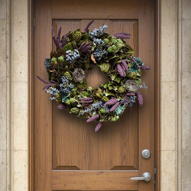 Decorative spring wreath with green leaves, purple flowers, and tiny nests hanging on a wooden front door.