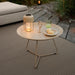 Beige round tray table with portable lamp, fruits and a glass, placed over a brown outdoor rug on a patio