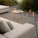 Outdoor patio with beige sectional sofa, brown outdoor rug, round tray table, and portable lamps surrounded by grasses