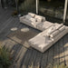 Wooden deck patio with L-shaped beige sectional sofa, brown outdoor rug, and two round tray tables by sliding glass wall