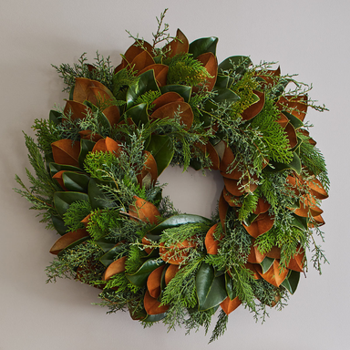 A festive wreath made of green leaves and evergreen branches, evoking a fresh winter scent with Carolina Sapphire Cypress.