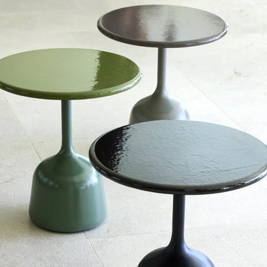Three round outdoor coffee tables in green, black, and gray, set on a concrete floor