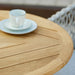 Close up of wooden top round outdoor cafe table with white cup and plates on top