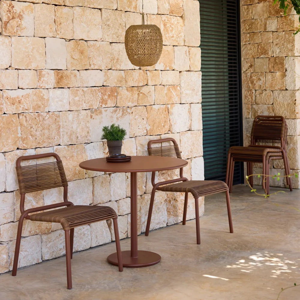 Brown round outdoor cafe table paired with two brown dining chairs set on a patio against stone brick wall