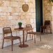 Brown round outdoor cafe table paired with two brown dining chairs set on a patio against stone brick wall