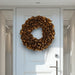 Glossy gold lacquer wreath displayed on a modern white front door with side glass windows.