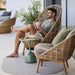 Boxhill's Glaze Outdoor Round Coffee Table lifestyle image at patio with a man sitting down on Hive Outdoor Highback Lounge Chair while holding a cup of coffee
