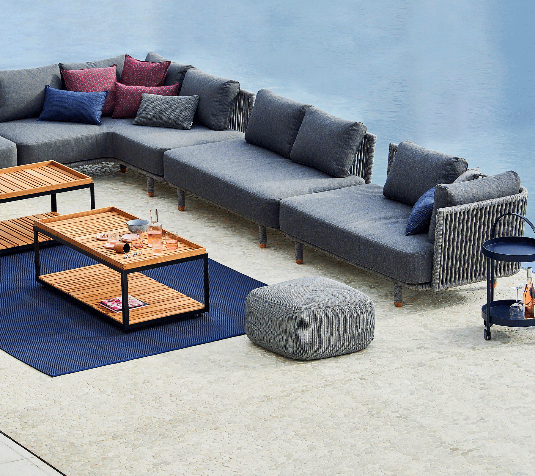Boxhill's Moments 2-Seater Left Module Sofa lifestyle image with other Moments Module Sofa Collection, 2 Level Coffee Table with Teak Top and a fabric footstool beside the pool