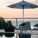 Boxhill's Kingston Outdoor Stackable Lounge Chair lifestyle image at poolside with parasol, black fabric footstool, and round side table