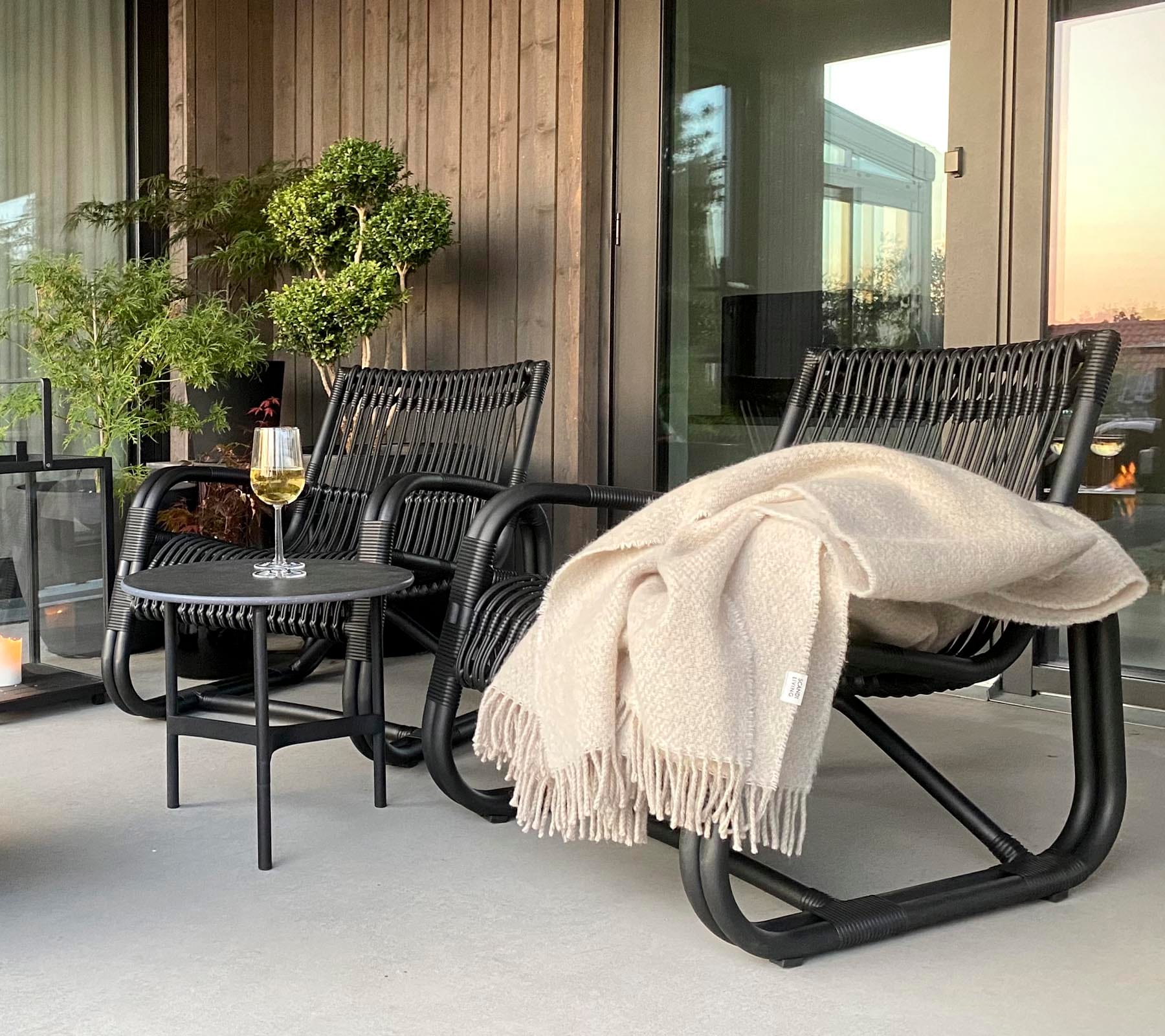 Boxhill's Curve Lounge Weave Outdoor Chair Graphite lifestyle image at patio with fabric cloth hanging on armrest and round side table
