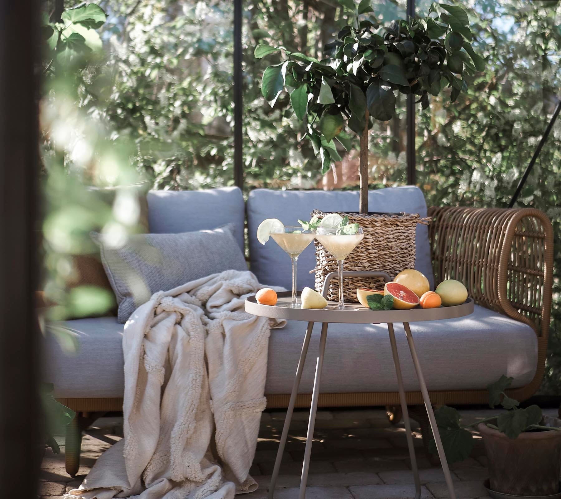 Boxhill's Nest 2-Seater Sofa lifestyle image at patio with small round table in front with fruits, cocktail and a plant on top