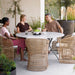 Boxhill's Joy Round Outdoor Dining Table Lifestyle image with dining chairs and 3 people sitting down having a chat