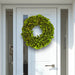 Bright green lacquer wreath with glossy finish on a modern white front door with glass panels.