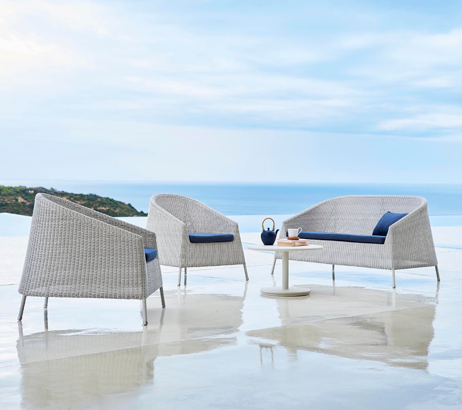 Boxhill's Kingston Outdoor Stackable Lounge Chair lifestyle image with Kingston Stackable Outdoor 2-Seater Sofa and white round table at seafront