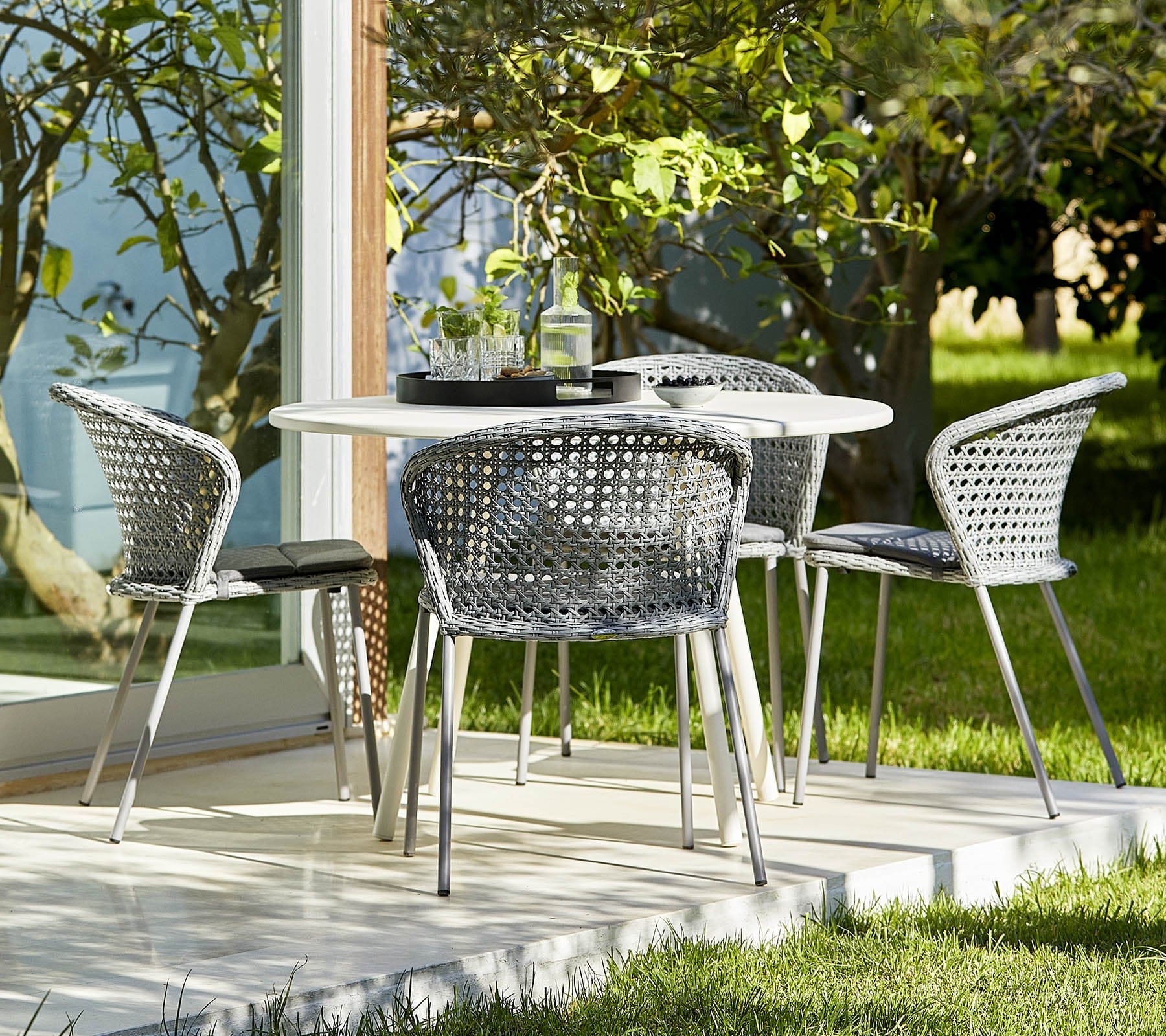 Boxhill's Lean Stackable Outdoor Garden Chair French Weave lifestyle image at patio with white round table and 2 glasses of water and a bottle container on top