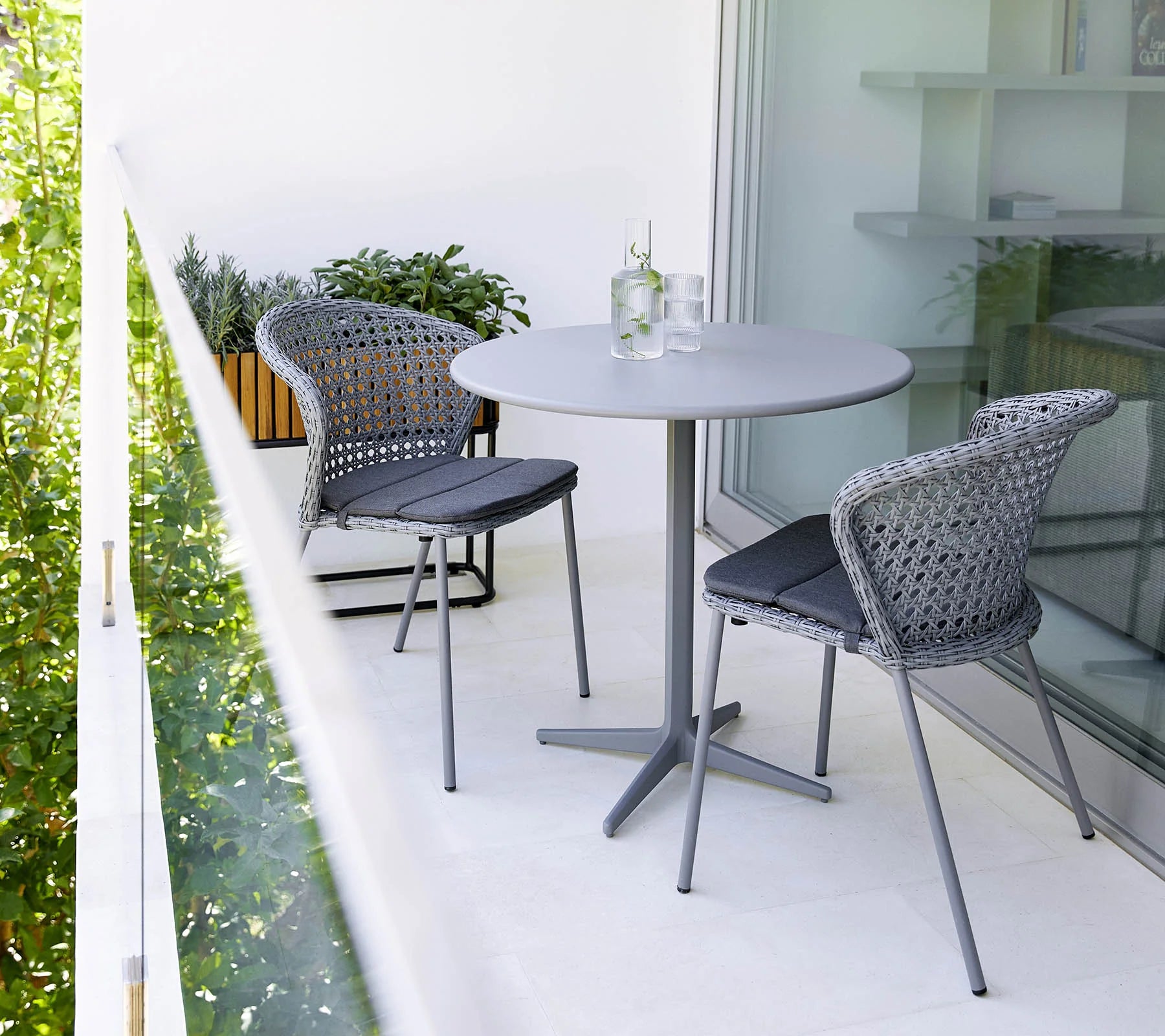 Boxhill's Lean Stackable Outdoor Garden Chair French Weave lifestyle image on balcony with round table and 2 glasses of water and a bottle container on top