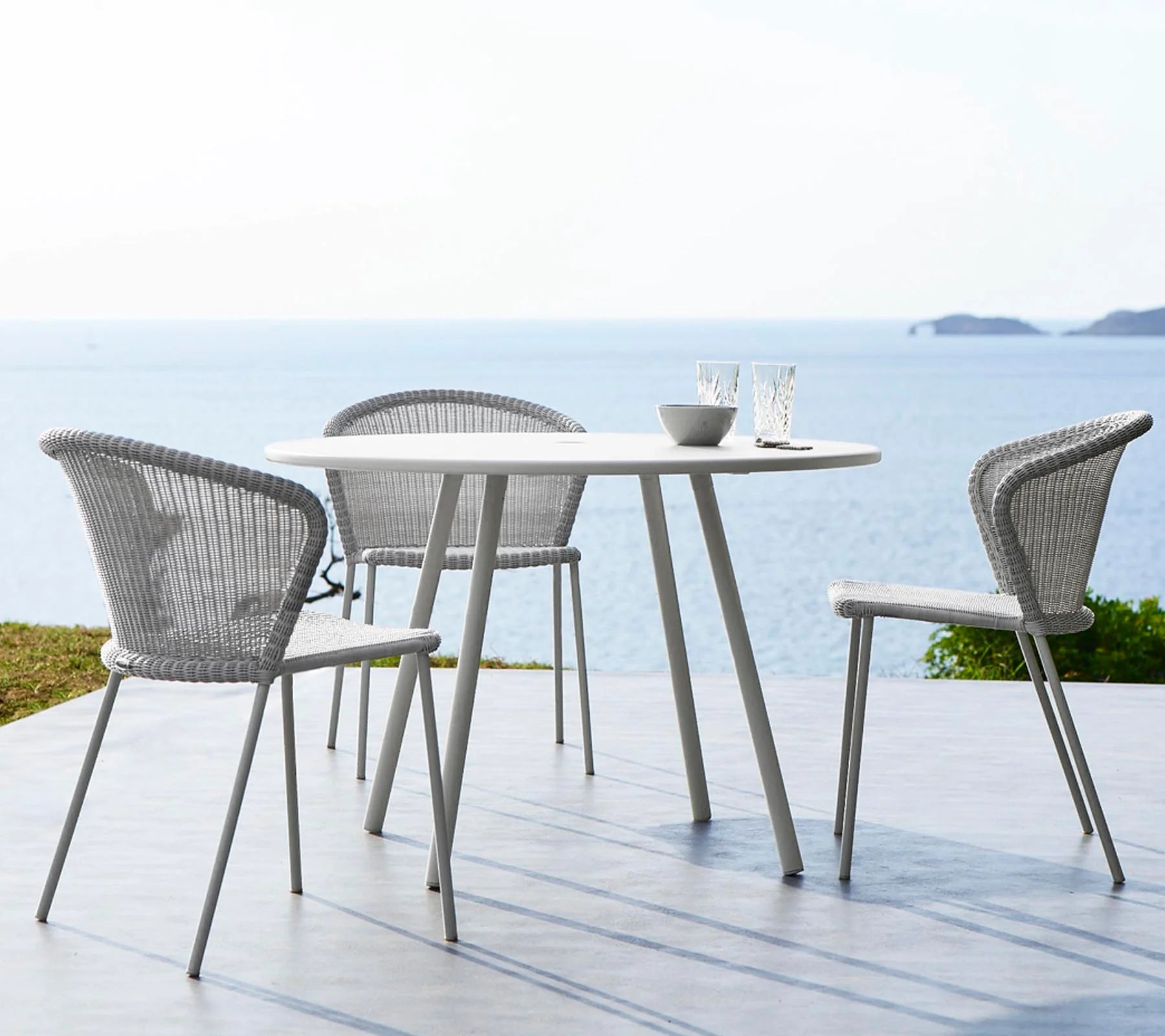 Boxhill's Lean Stackable Outdoor Garden Chair White Grey lifestyle image at seafront with white round table and 2 glasses and a bowl on top