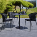 Boxhill's Lean Stackable Outdoor Garden Chair Black Weave lifestyle image at patio with black round table and 2 cups and a pot on top