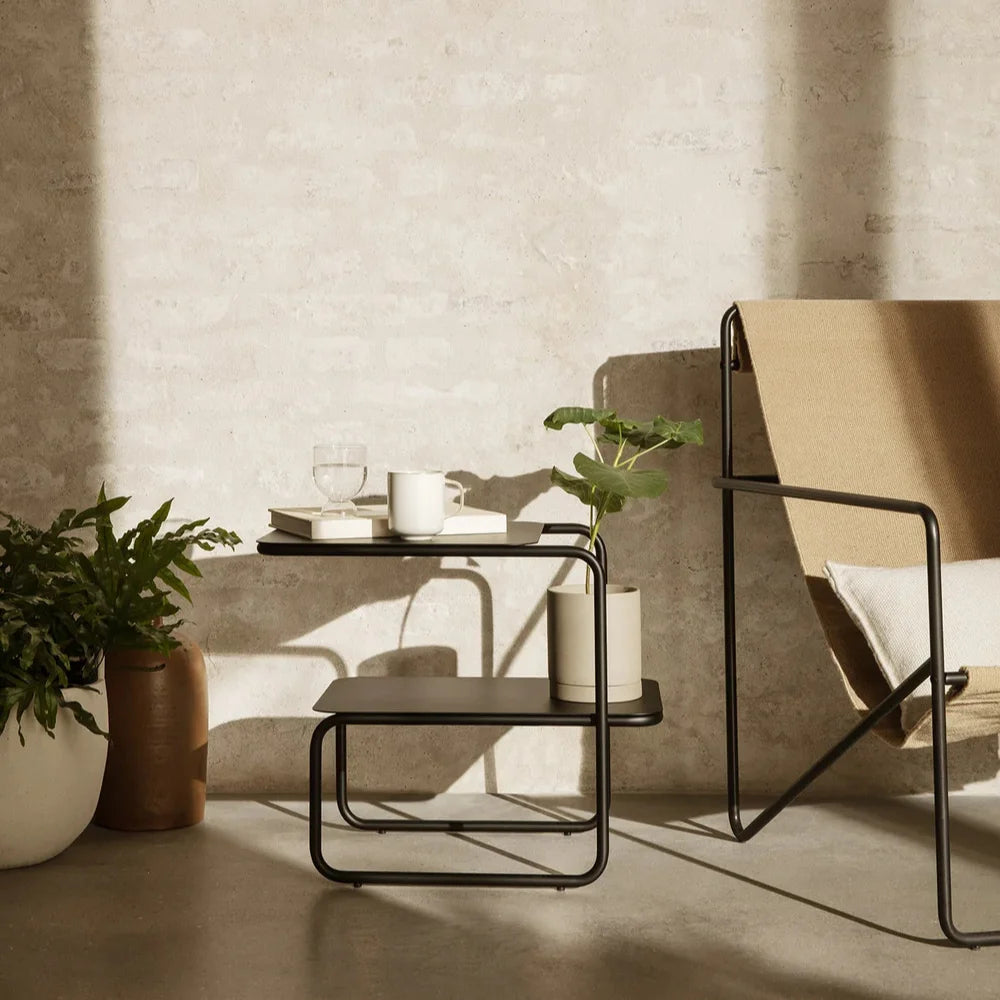 Modern interior with a beige chair, small table, and potted plants against a textured wall.