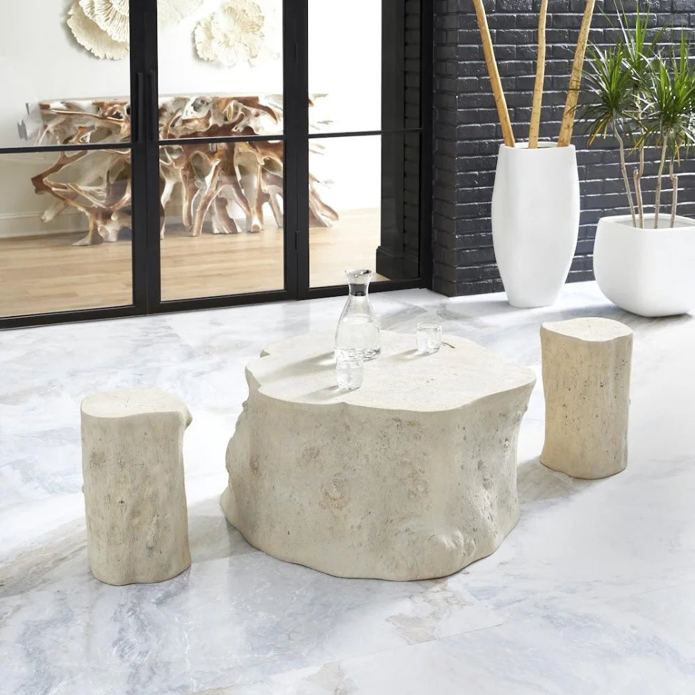 A rustic three-piece furniture set featuring a natural stone coffee table and two matching log stools in a modern, light-filled room.