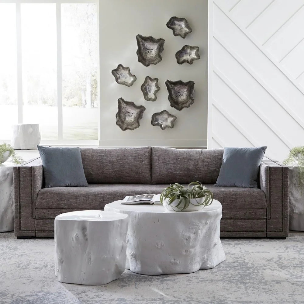 A modern living room scene featuring a textured gray fabric sofa with slate blue pillows, a white tree-stump coffee table, and matching decorative wall art.