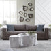 A modern living room scene featuring a textured gray fabric sofa with slate blue pillows, a white tree-stump coffee table, and matching decorative wall art.