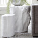Two white faux log side tables in a modern living room setting, with one smaller cylindrical table in front of a larger rectangular table topped with a hanging plant.